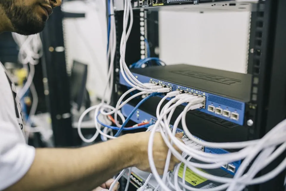 Un technicien analyse le câblage et le switch d'une baie réseau